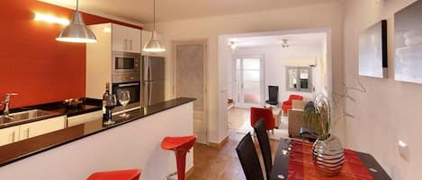 A modern kitchen with a dining area, red bar stools, and a dining table with a vase.
