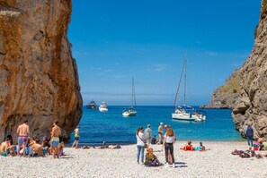 A rocky beach with people sunbathing and swimming, boats in the water, and a clear blue sky. - Fabulous situation, townhouse in Pollensa, Gruat. (Pollensa / Pollença)