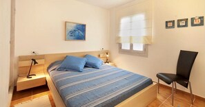 Une chambre à coucher comprenant un lit, des tables de chevet, une chaise, une fenêtre avec des stores et des œuvres d’art murales.
