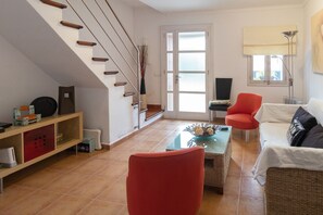 Un salon avec un escalier, un fauteuil rouge, un canapé blanc, une table basse et une bibliothèque.