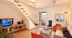Un salon moderne avec un téléviseur, un escalier, un fauteuil rouge et une lampe sur pied.
