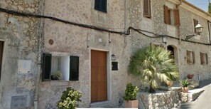 A stone building with a wooden door, shutters, and a small balcony with plants.