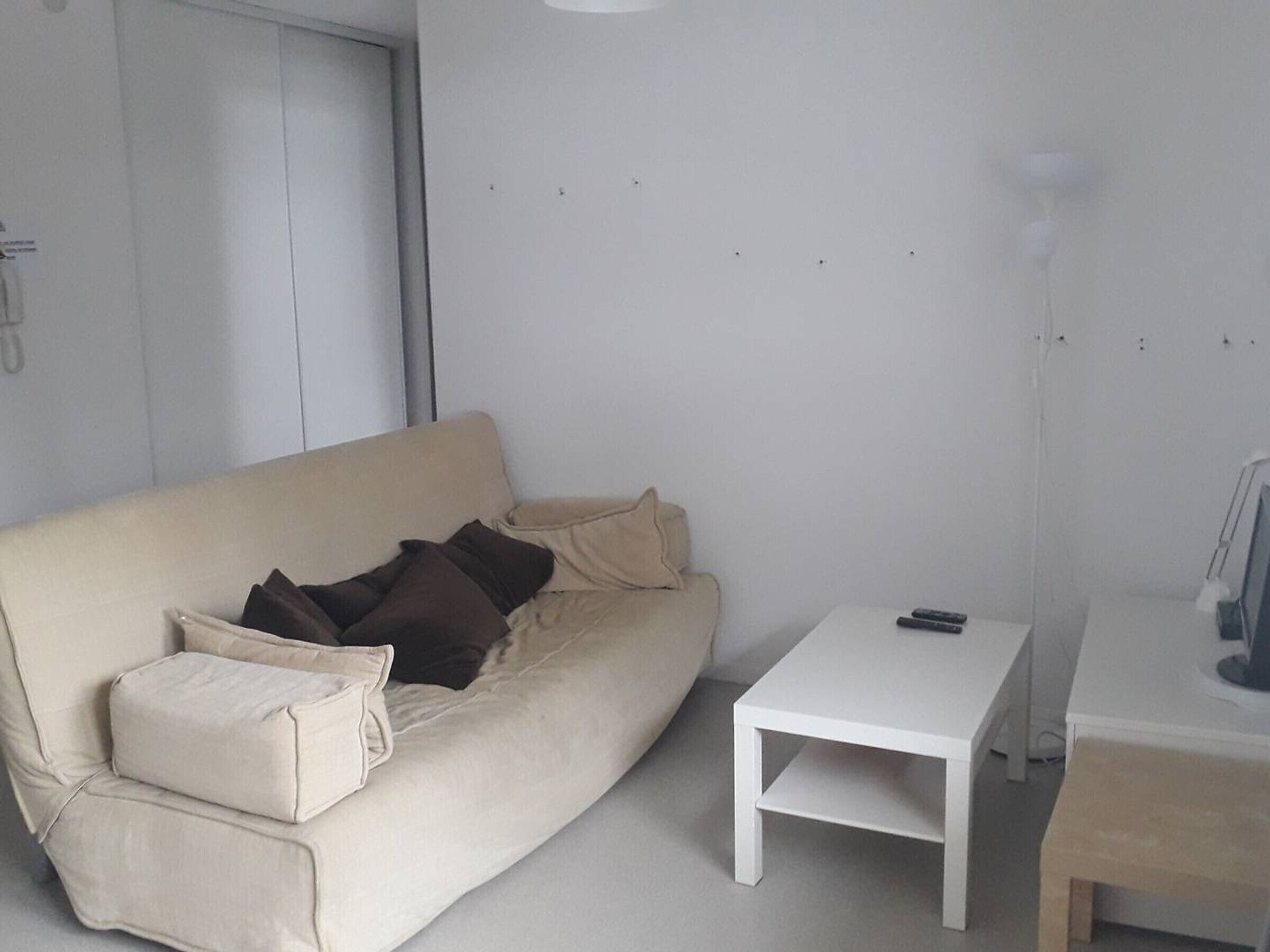 Un salon minimaliste avec un canapé beige, une table basse blanche et une lampe.