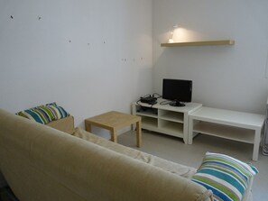 Relax in this serene living space with a beige sofa, flat-screen TV, and a wall-mounted shelf.