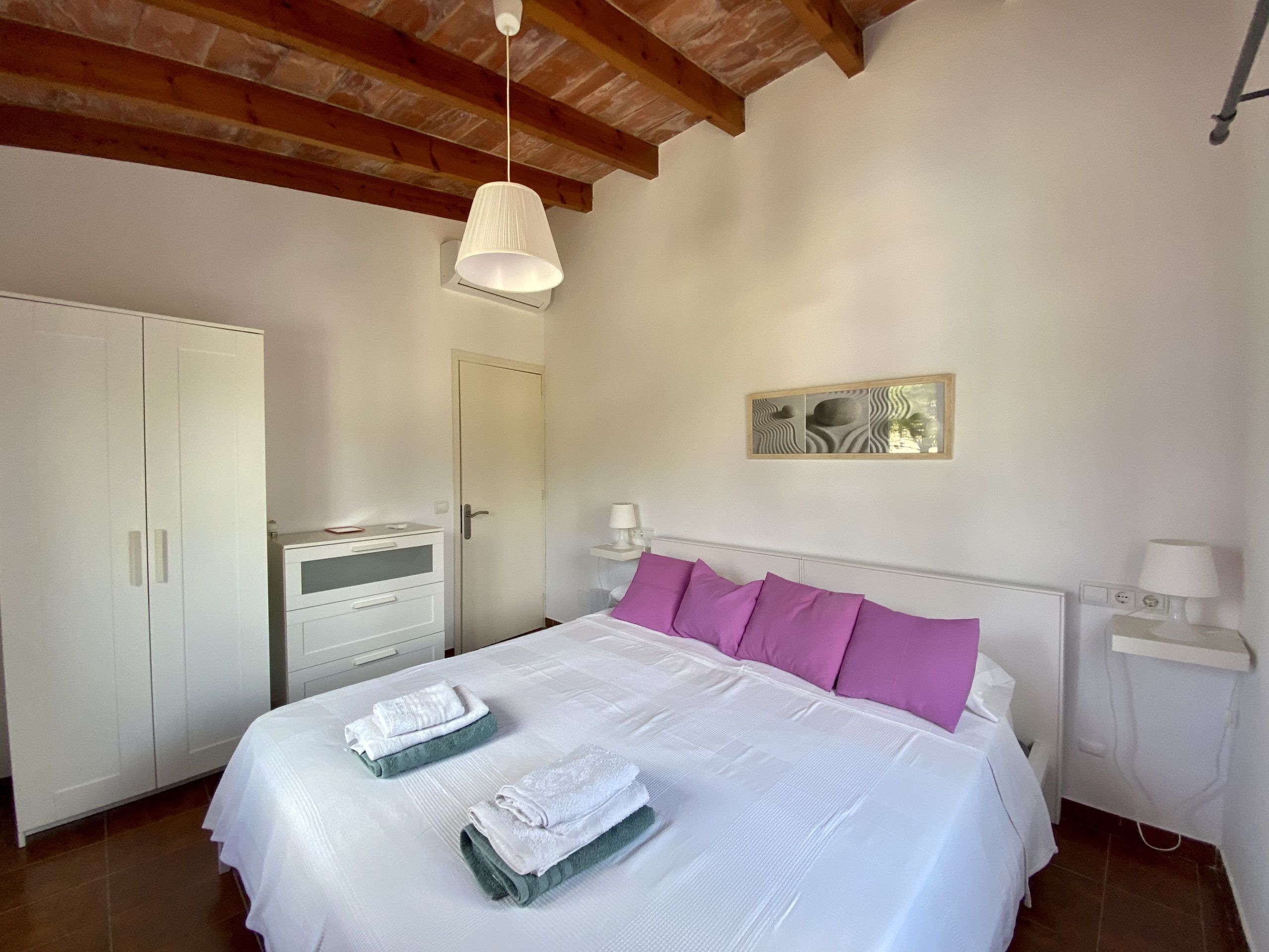 Un dormitorio con cama, armario, mesita de noche y lámpara colgante.
