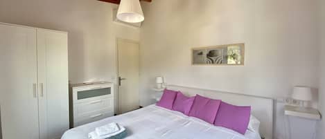 Une chambre à coucher comprenant un lit, une armoire, une table de chevet et un luminaire suspendu.