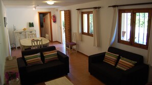Un salon avec deux canapés noirs, une table à manger avec des chaises et un coin cuisine visible à travers une porte ouverte.
