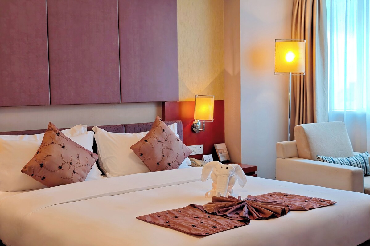Une chambre d’hôtel avec un grand lit, des oreillers, une table de chevet, une lampe et une chaise.