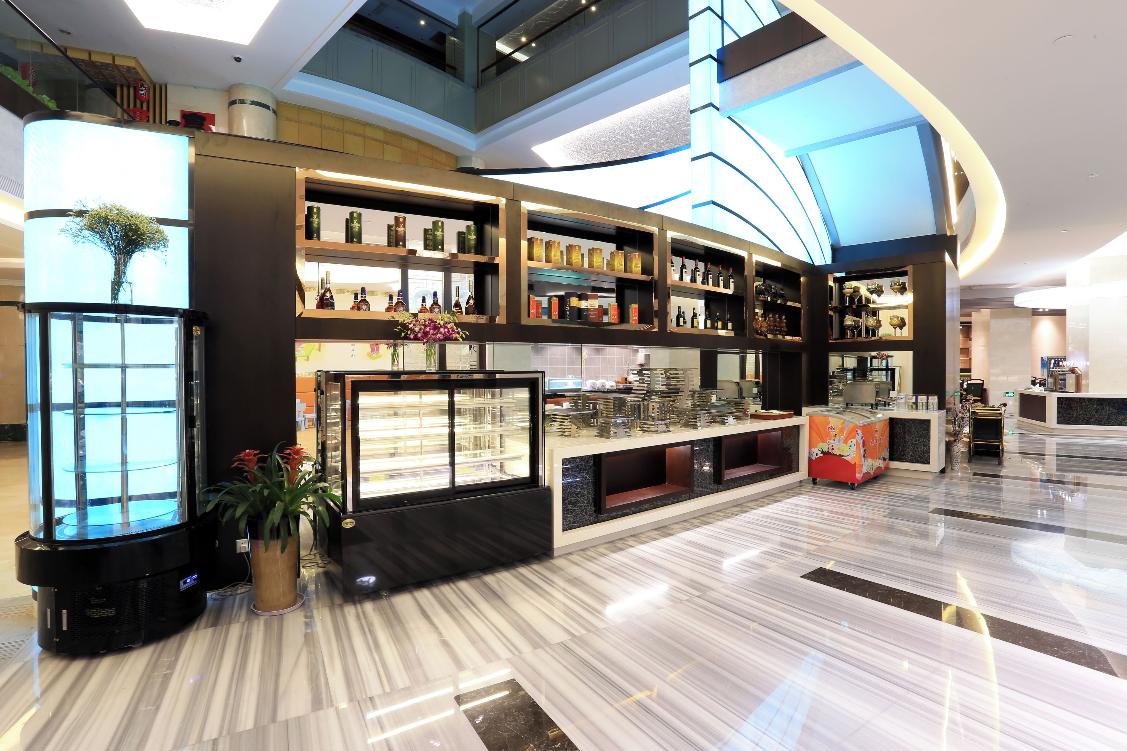 A modern hotel lobby with a marble floor, a central display case, and a curved ceiling design.
