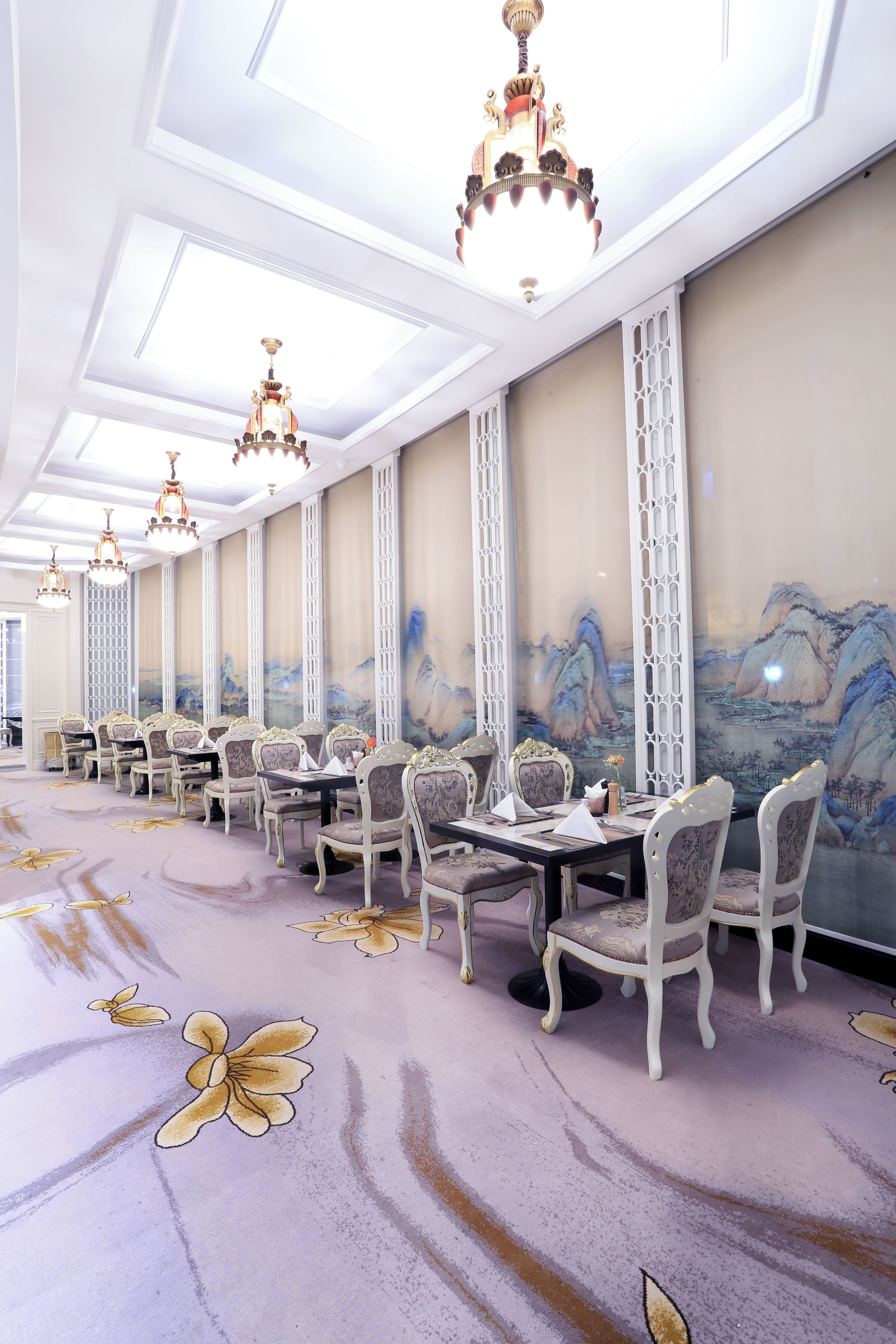 A banquet hall with long tables, ornate chandeliers, and traditional wall paintings.