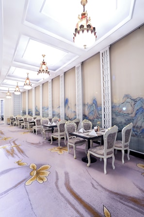 Un salón de banquetes con mesas largas, candelabros ornamentados y pinturas murales tradicionales.