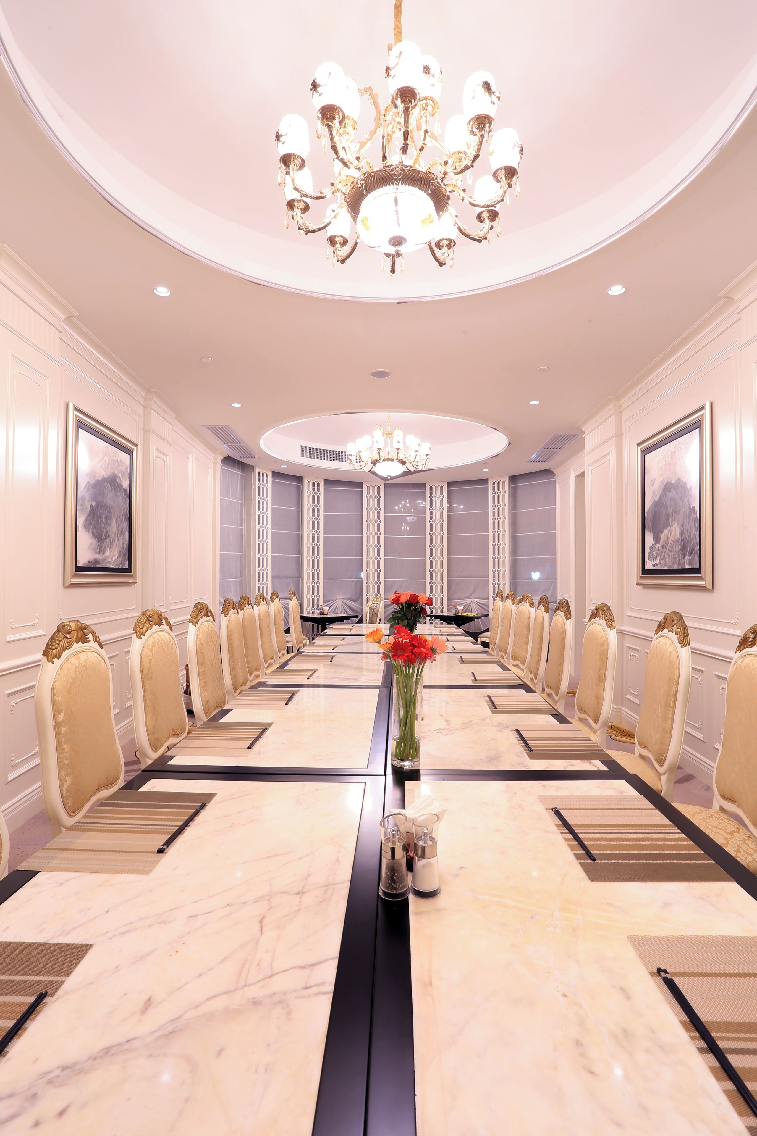 A conference room with a long table, chairs, a chandelier, and framed artwork on the walls.