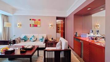 A hotel room with a sofa, a dining table, a small bar area, and a decorative wall piece.