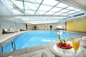 An indoor swimming pool with a glass ceiling, lounge chairs, and a table with a drink and fruit. - Xiamen Jingmin Central Hotel (Xiamen)