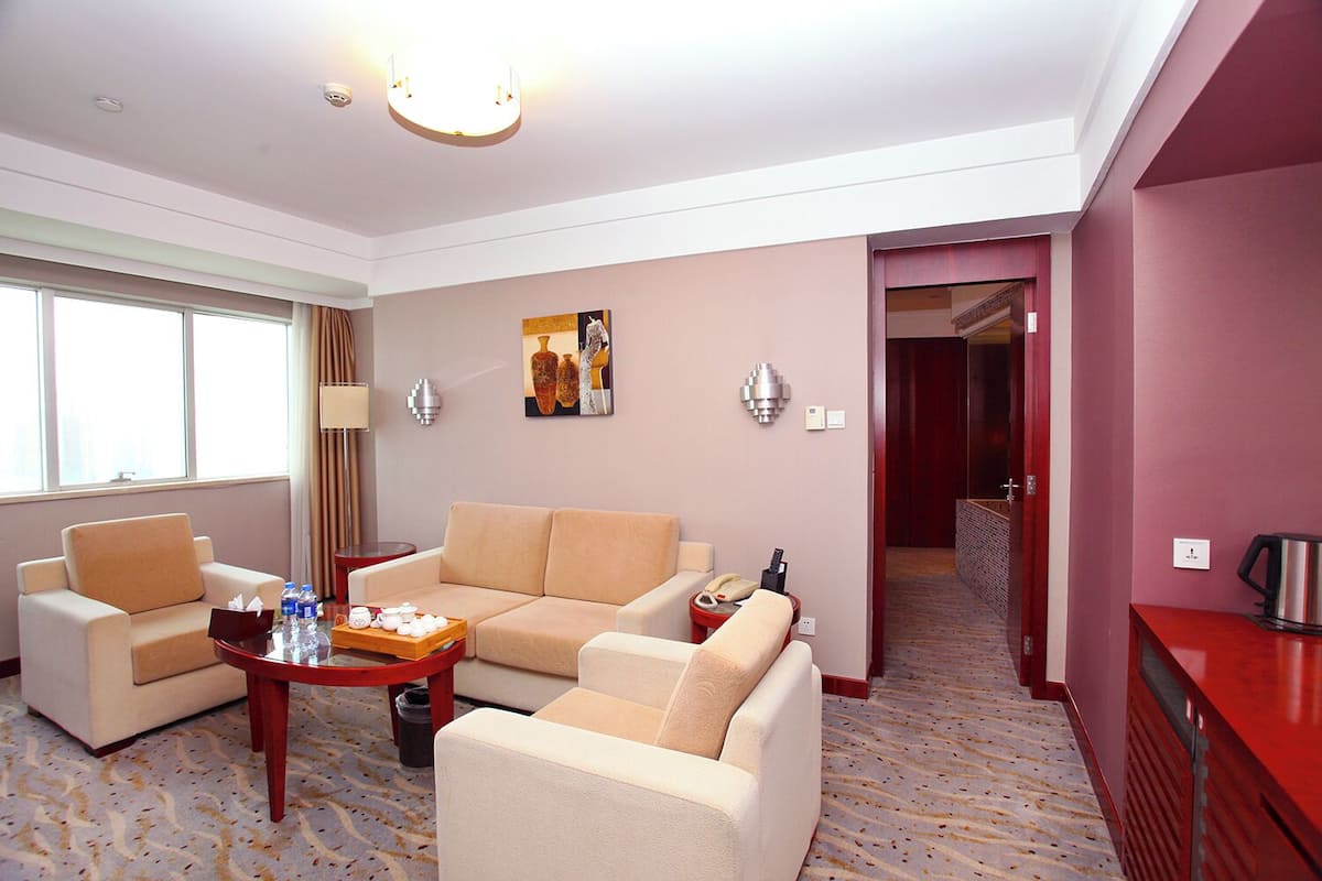 Une chambre d’hôtel comprenant un canapé, une table basse avec un plateau contenant du thé et des bouteilles d’eau, un téléphone et un buffet rouge avec une bouilloire.