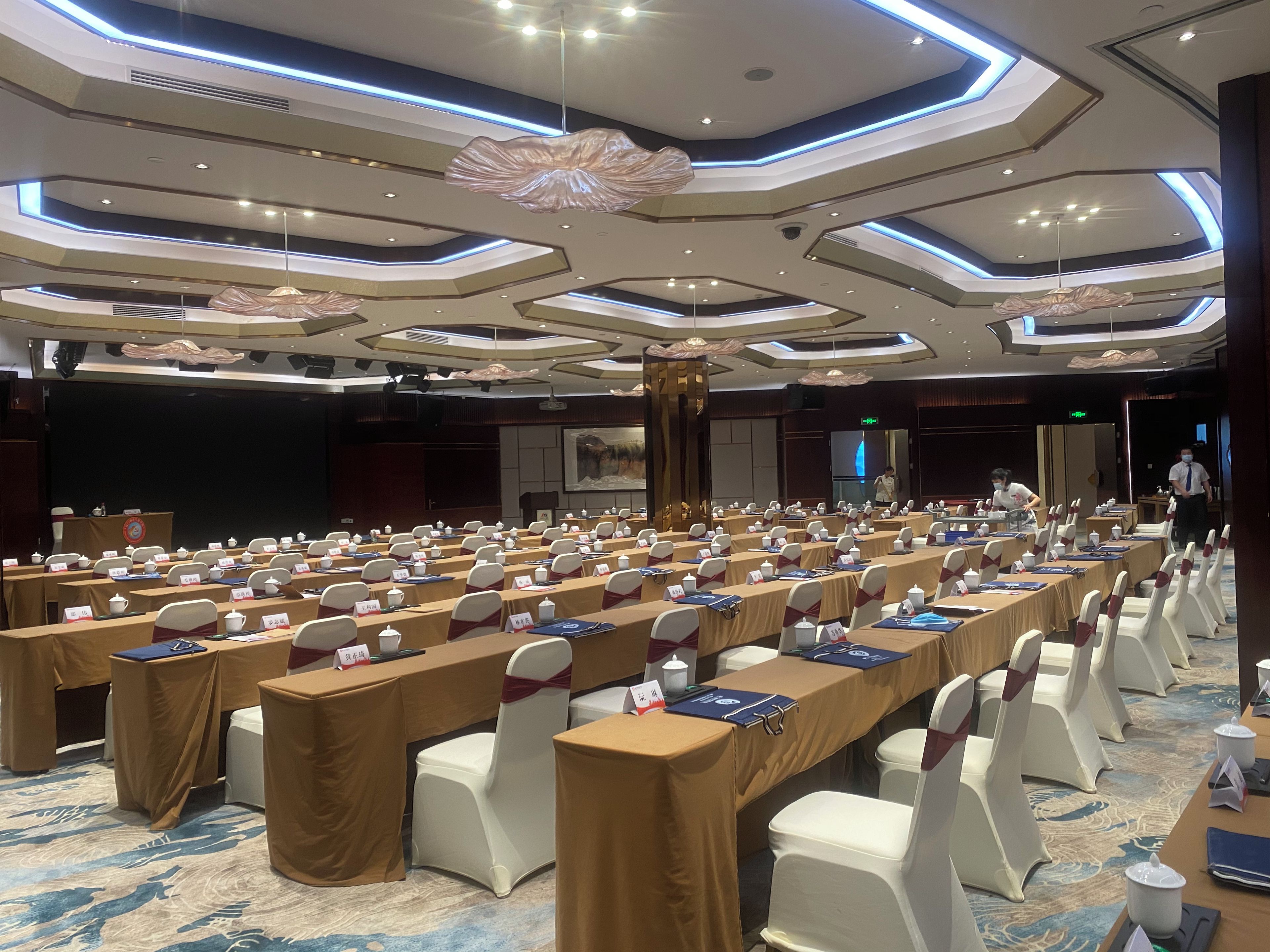 A conference room with rows of tables, chairs, and nameplates, equipped with microphones and laptops.