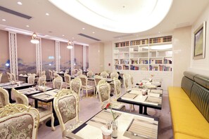 A dining area with tables set for service, ornate chairs, and a bookshelf filled with books. - Xiamen Jingmin Central Hotel (Xiamen)