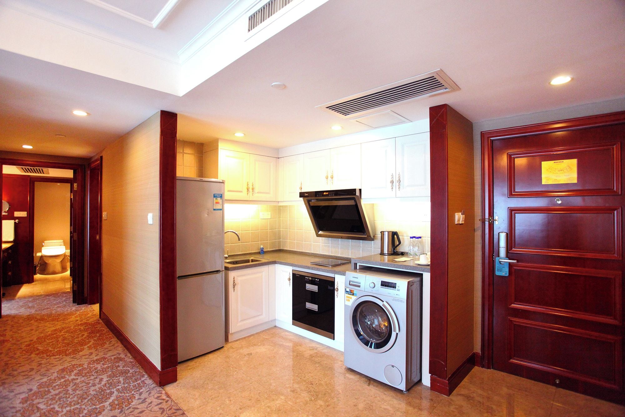 A compact hotel kitchen with a refrigerator, microwave, dishwasher, and washing machine.
