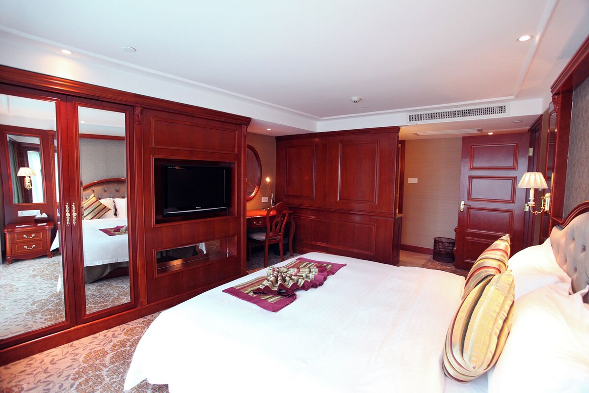 Une chambre d’hôtel avec un grand lit, une télévision, un bureau avec une chaise, un miroir et une armoire.