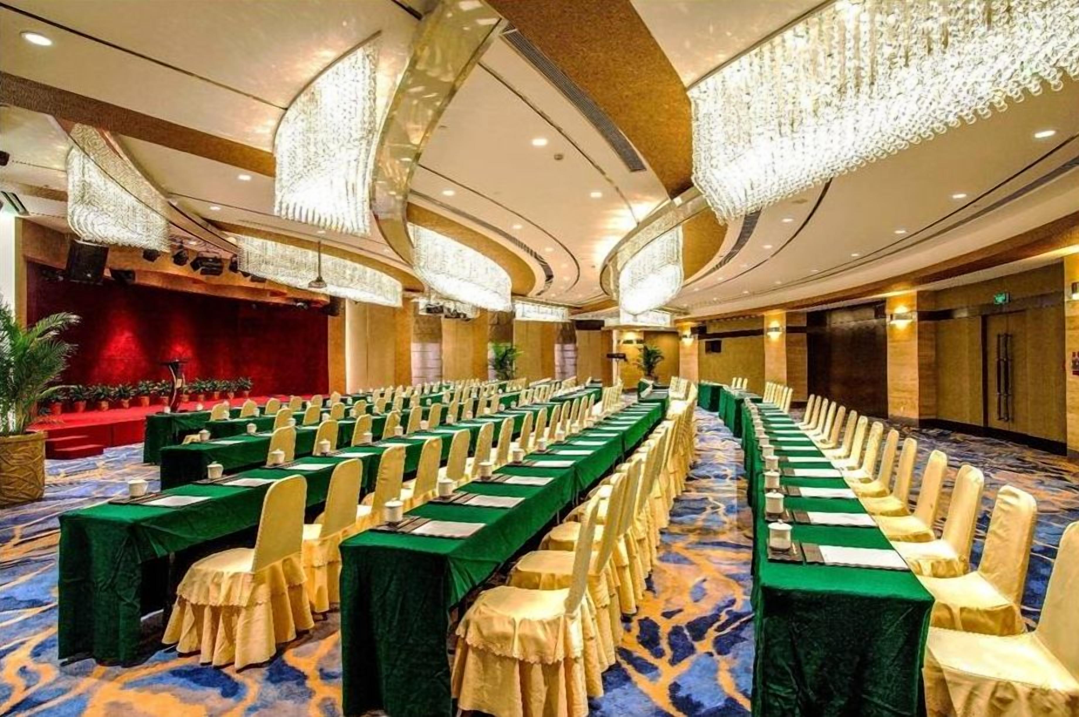 Un salón de conferencias con mesas largas, sillas y un escenario.