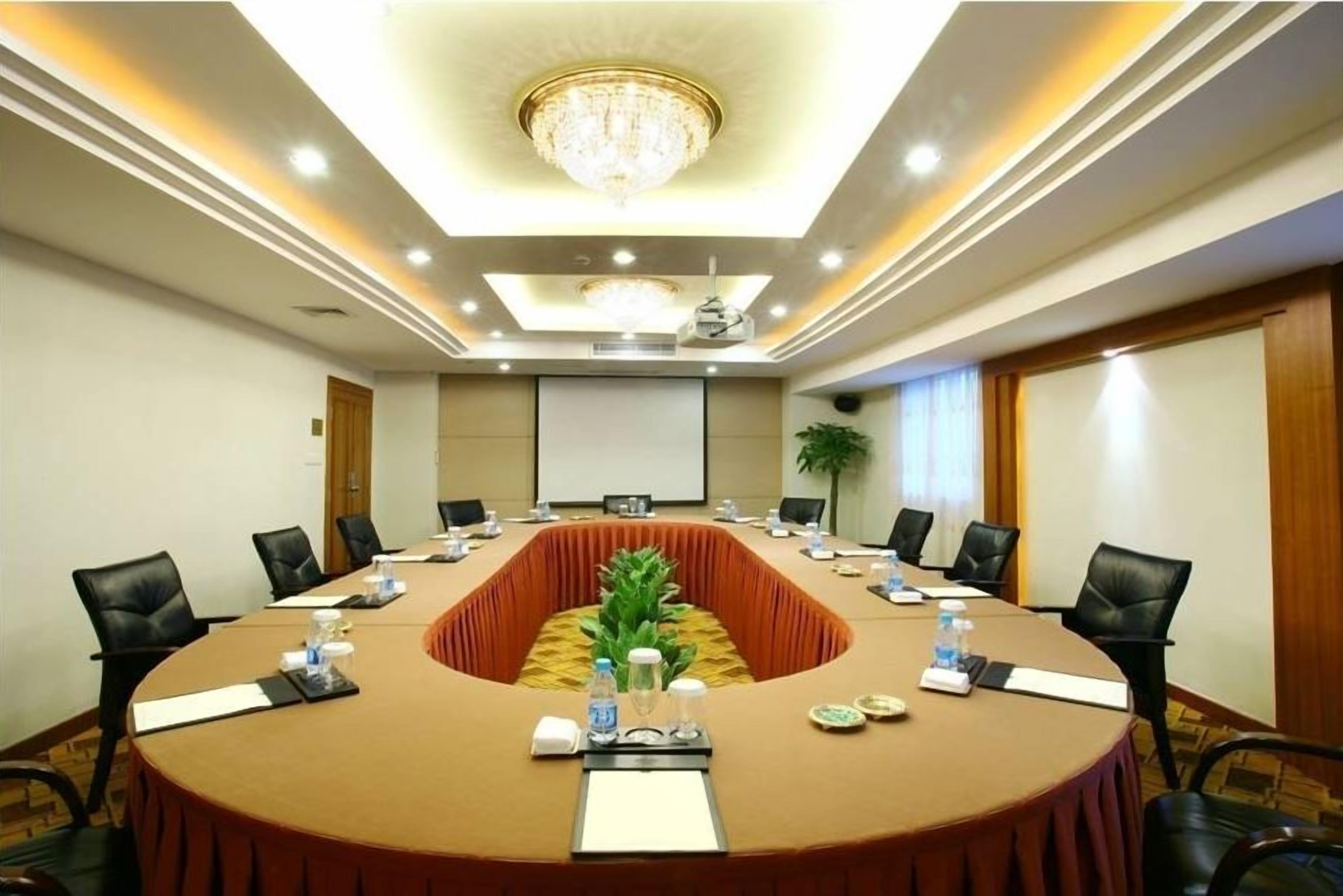 A conference room with a long table, black chairs, a chandelier, and a plant.