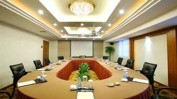 A conference room with a long table, black chairs, a chandelier, and a plant.