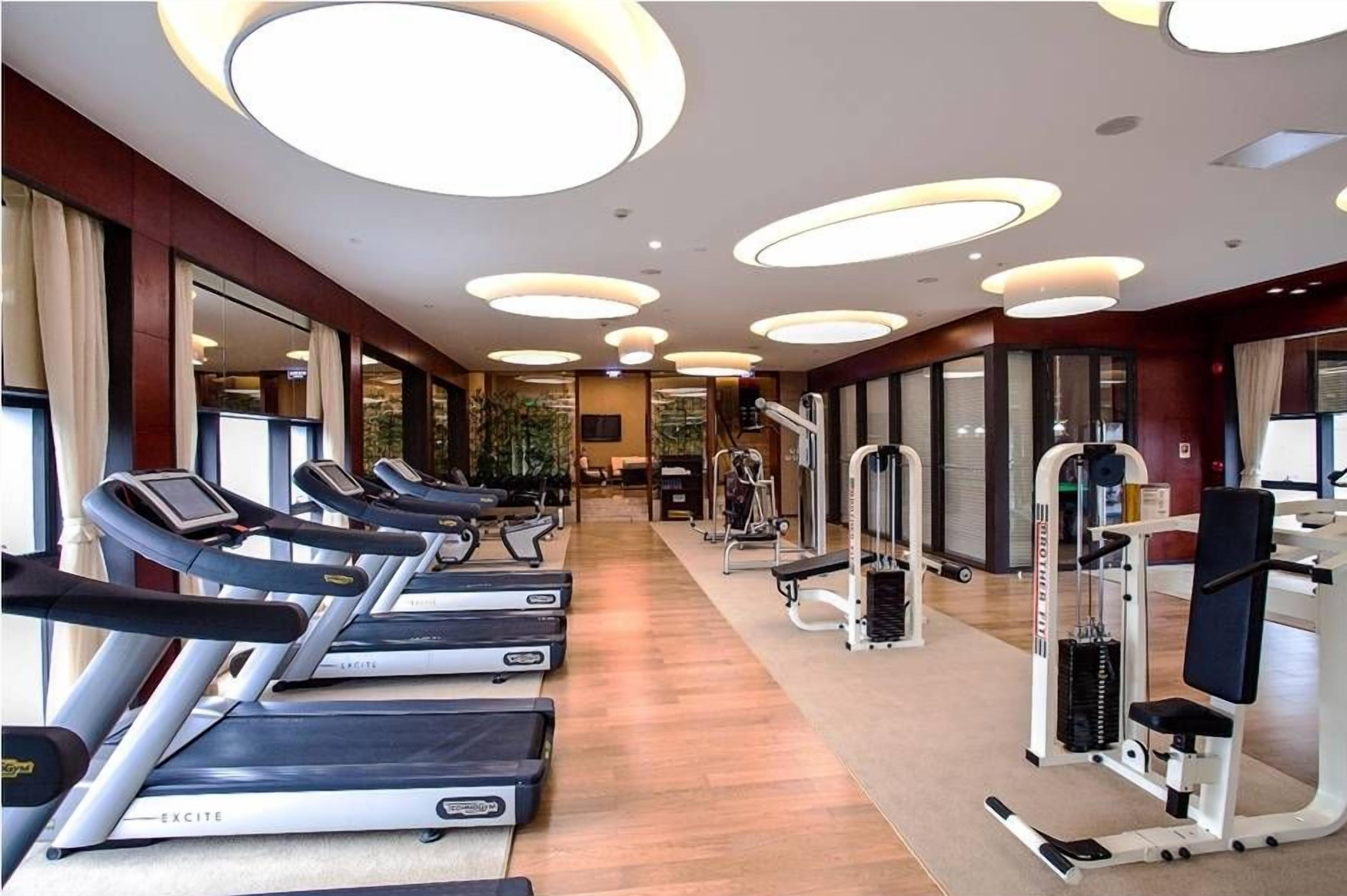 A gym with treadmills, weight machines, and a mirror wall.