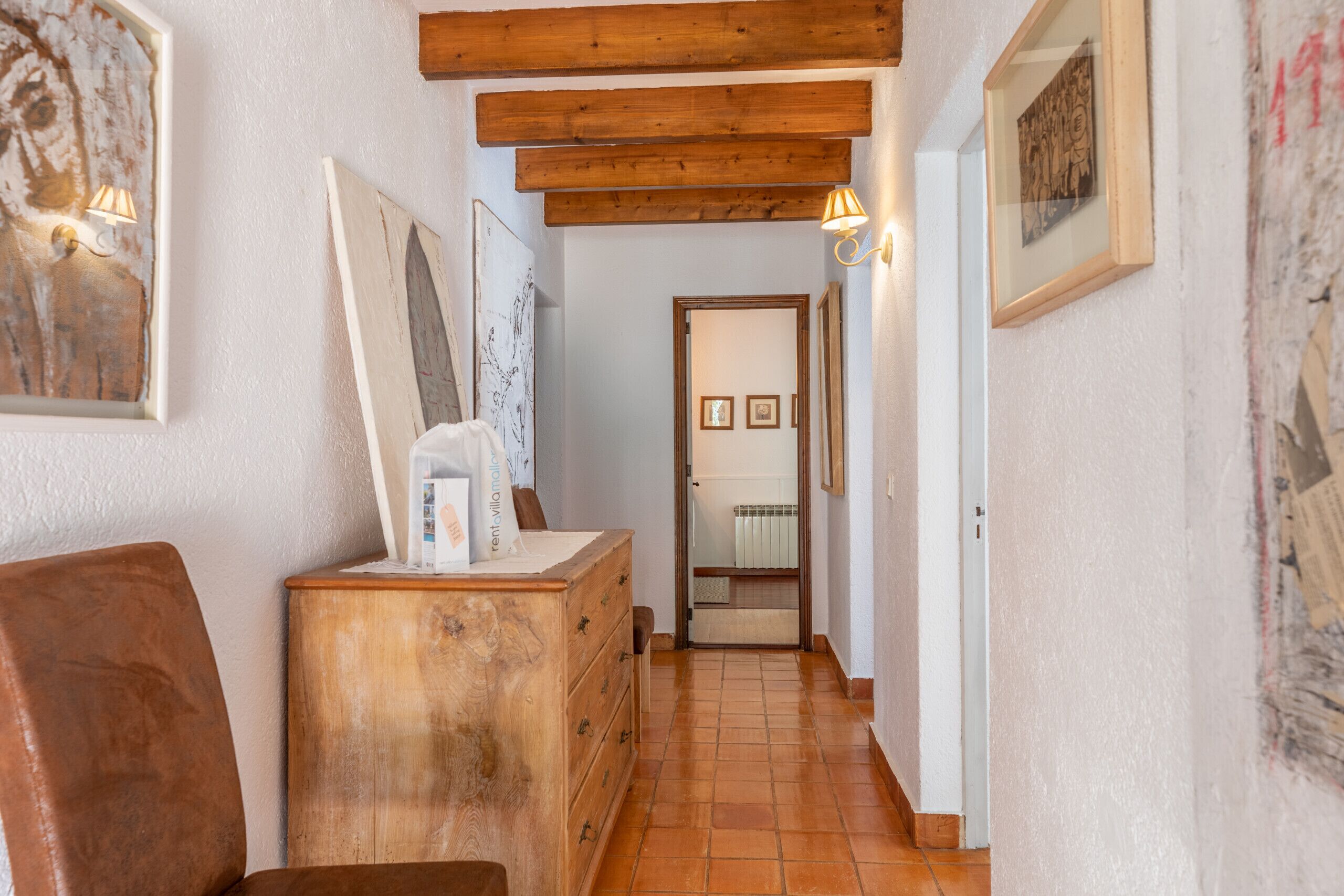 Un pasillo con vigas de madera, un sillón de cuero marrón, un aparador de madera y obras de arte enmarcadas en las paredes.