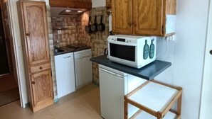 A compact kitchen with wooden cabinets, a white microwave, and a small refrigerator.