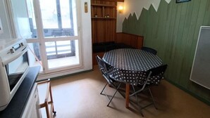 A small room with a round table and chairs, a kitchenette, and a sliding glass door leading to a balcony.