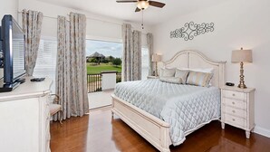 Une chambre à coucher comprenant un lit, une télévision, une commode, une table de chevet et un balcon avec des rideaux.