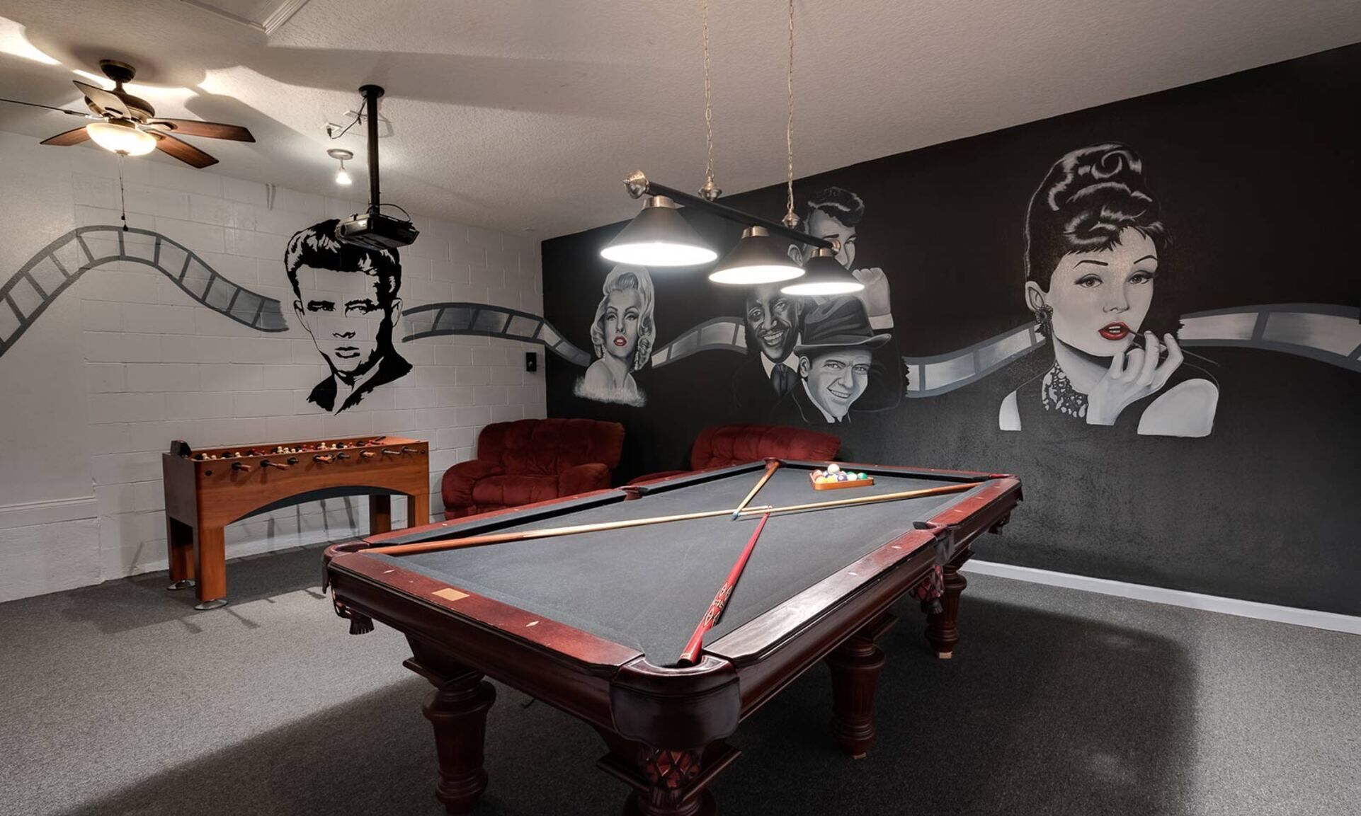 Ein Billardraum mit Pooltisch, roten Stühlen, einem Tischfußballspiel und einem Wandgemälde.