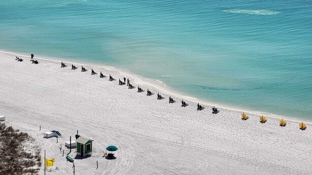 A beach with a row of sun loungers and a small structure, likely a lifeguard station, on the sand.
