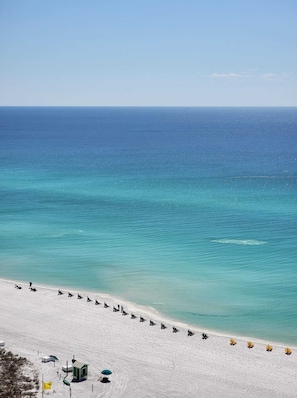 A beach with a row of sun loungers and a small structure, likely a lifeguard station, on the sand. - Book 3 Nights, Get 1 Free (See Description) | 16th-Floor Gulf View & 6-Seat Cart (Miramar Beach)