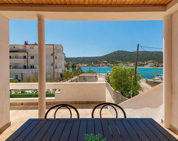 A balcony with a view of a coastal town, a table, and chairs.