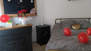 Quarto com cama, penteadeira, lousa e prateleira na parede com três objetos pretos.