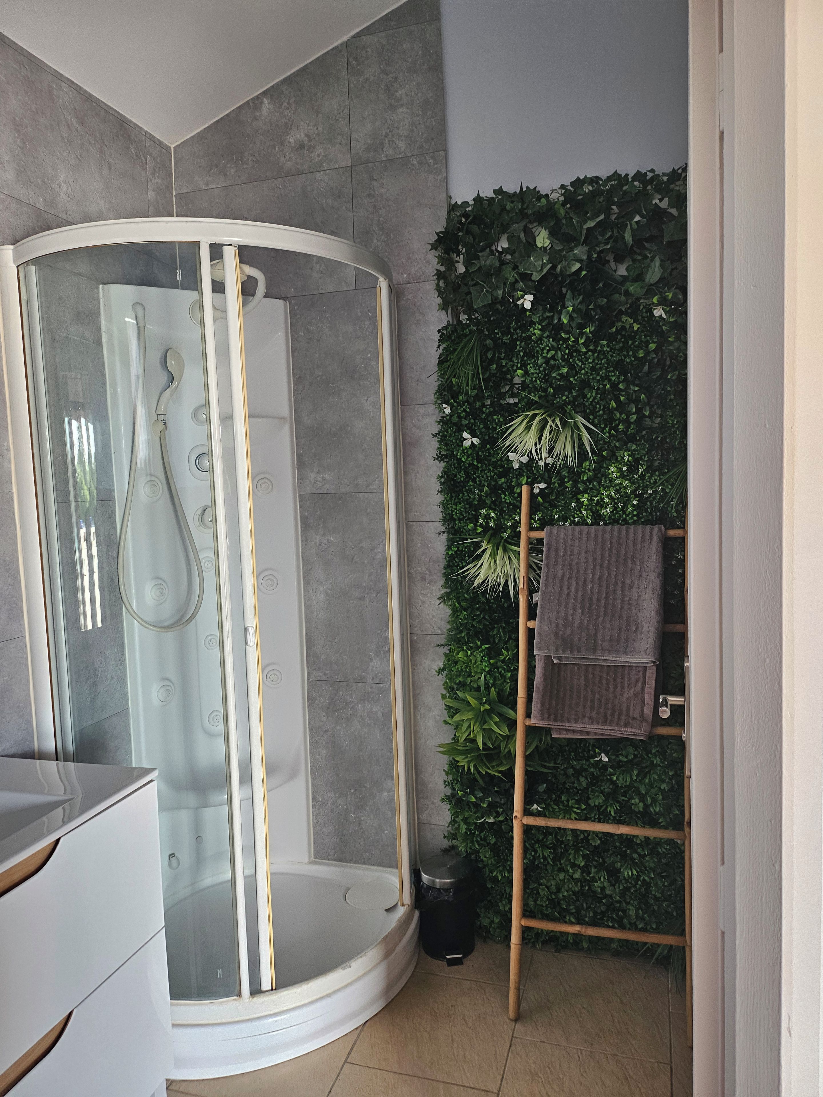 A modern bathroom with a glass-enclosed shower, a wooden towel rack, and a green plant wall.
