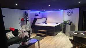 Quarto moderno com sofá preto, uma pequena mesa com um vaso de flores, uma banheira de hidromassagem e um refrigerador.
