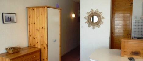 Una habitación pequeña y funcional con un armario de madera, una mesita con una silla y un espejo en la pared.