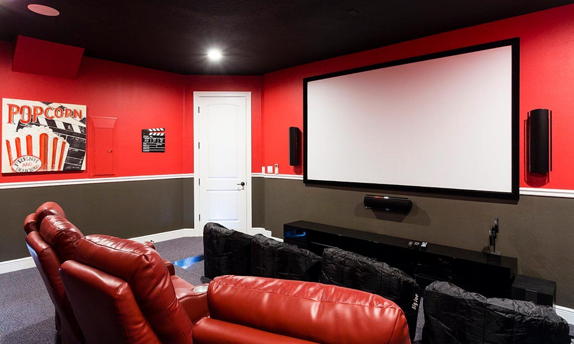 Ein Heimkino mit roter Wand, einer großen Leinwand und einem bequemen, rot-ledernen Sessel.