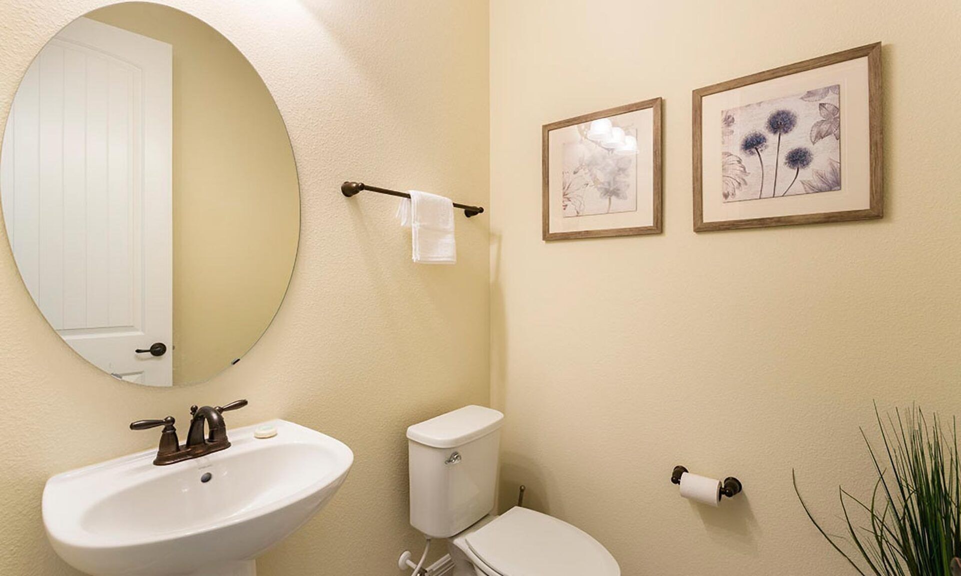 A bathroom with a round mirror, a sink, a toilet, and two framed floral pictures on the wall.