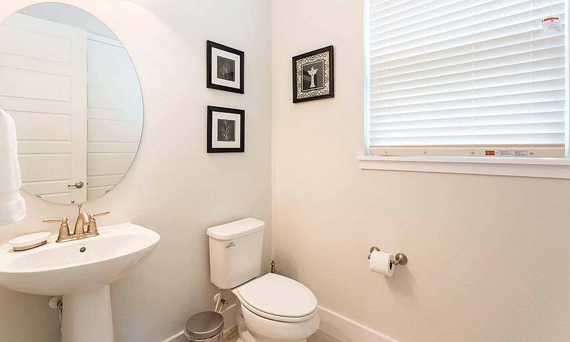 A bathroom with a white sink, toilet, and bidet, a mirror, and two framed pictures on the wall.
