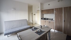 A modern kitchen with wooden cabinets, a dining table with chairs, and a grey sofa.