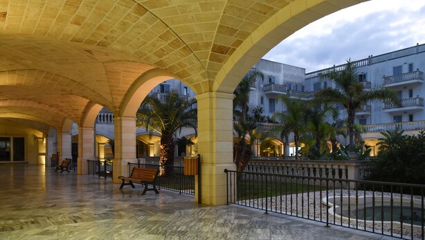 A spacious courtyard with arches, a fountain, and palm trees.