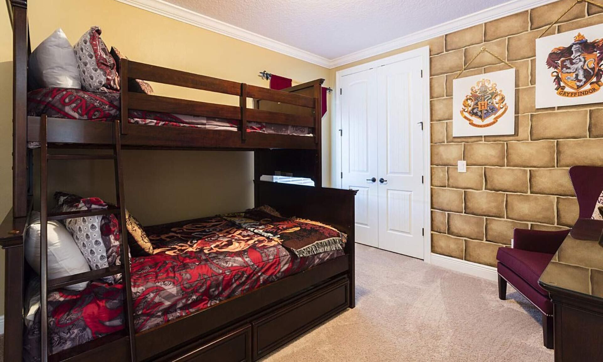 A bunk bed with patterned bedding, a door, a wall-mounted coat of arms, and a plush armchair.