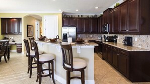 A kitchen with dark wood cabinets, a central island with bar stools, a refrigerator, and a microwave. - Beautiful 5 Star Villa on Reunion Resort and Spa with Large Private Pool, Orlando Villa 4597 (Orlando)