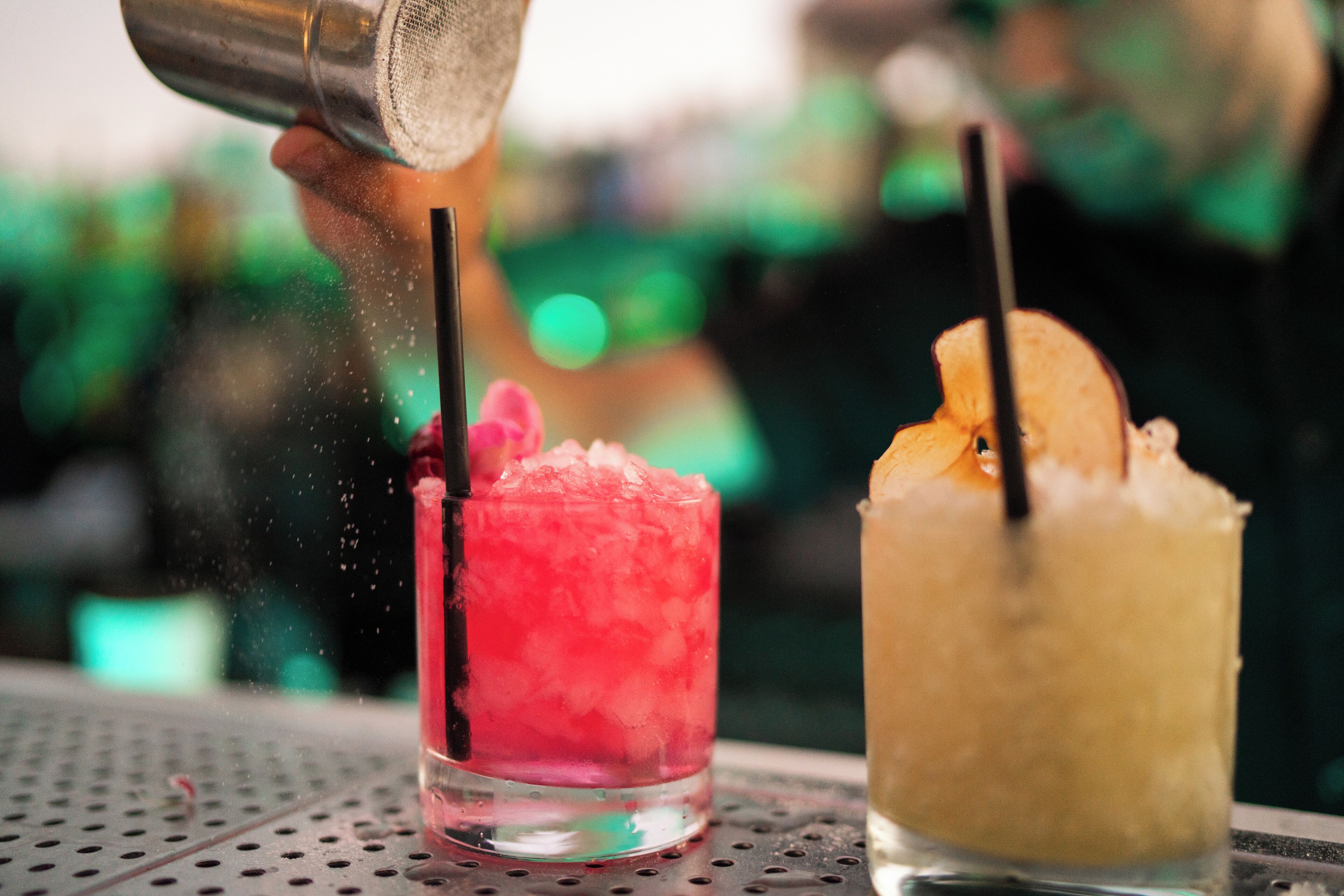 Deux cocktails servis avec des pailles, l’un contenant une boisson rose et l’autre une boisson jaune, sont versés à partir d’un shaker.