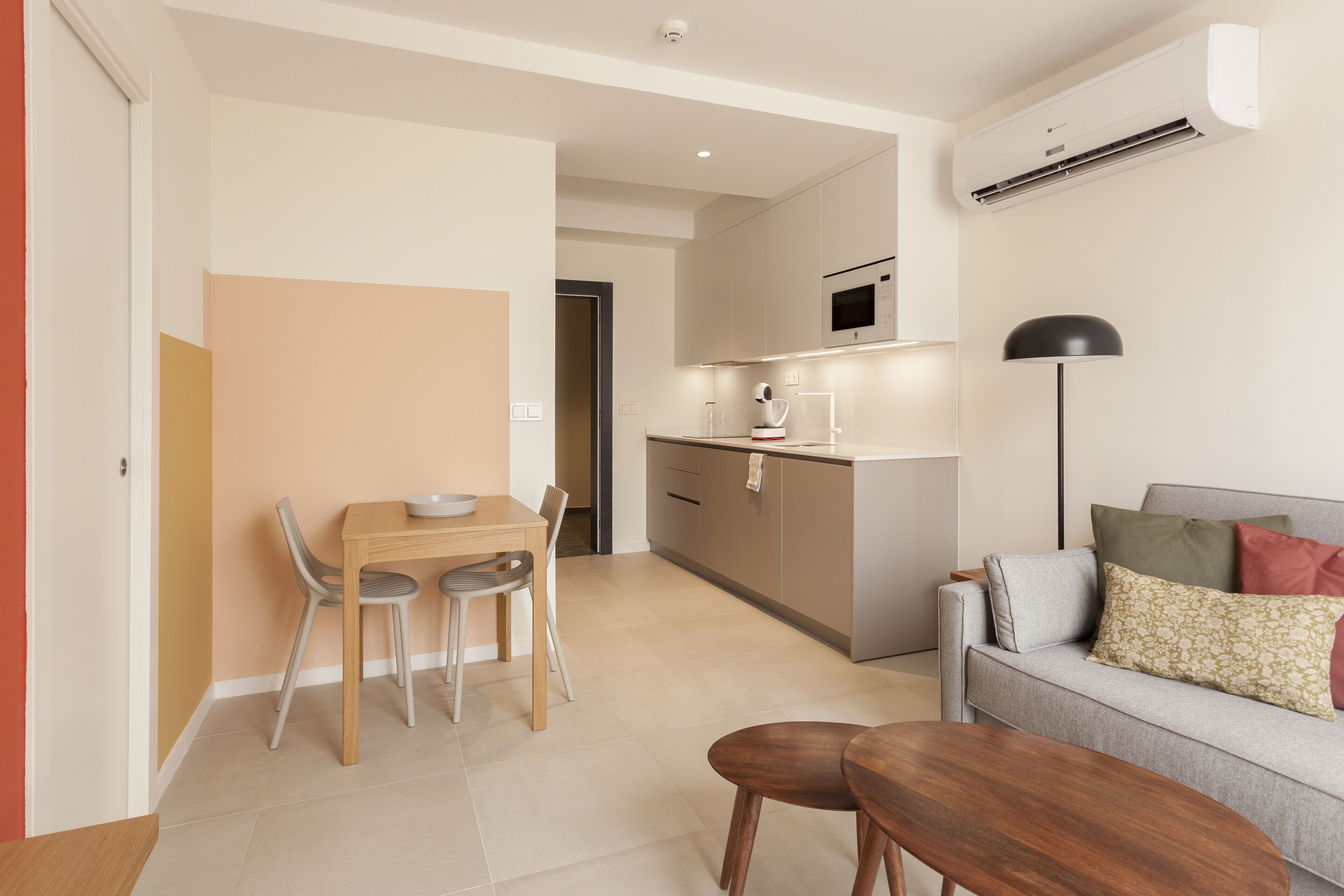 A modern living room with a sofa, a dining table with chairs, and a kitchen area with an air conditioner and microwave.