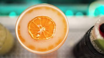 Un vaso de bebida anaranjada con una rodaja de naranja en el borde, sobre una superficie con fondo desenfocado.
