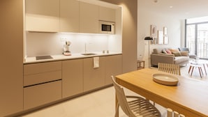 A modern kitchen with integrated appliances, a dining area with a wooden table and chairs, and a living room with a sofa and a coffee table. - Apartamentos Málaga Premium - Calle Granada (Málaga)